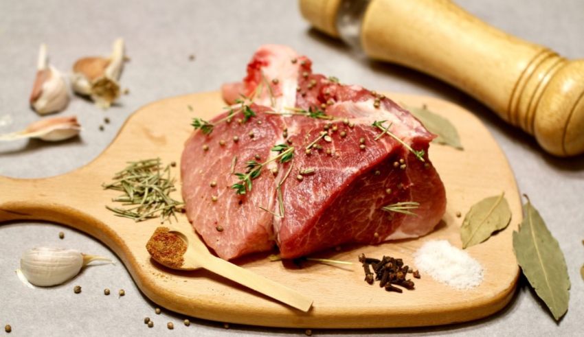 A piece of meat on a cutting board with herbs and spices.
