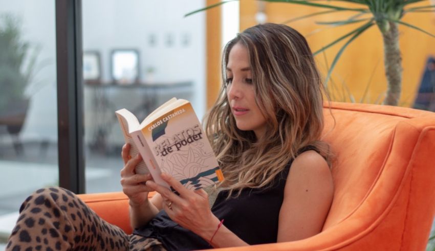 A woman sitting in an orange chair reading a book.