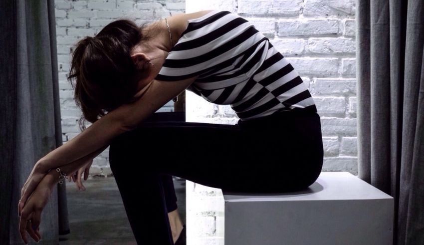 A woman sitting on a white cube with her head down.