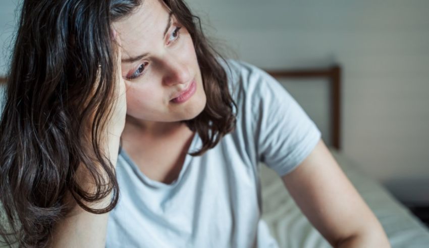 A woman is sitting on a bed with her head in her hands.
