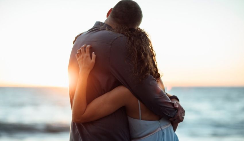 A man and woman hugging on the beach at sunset.