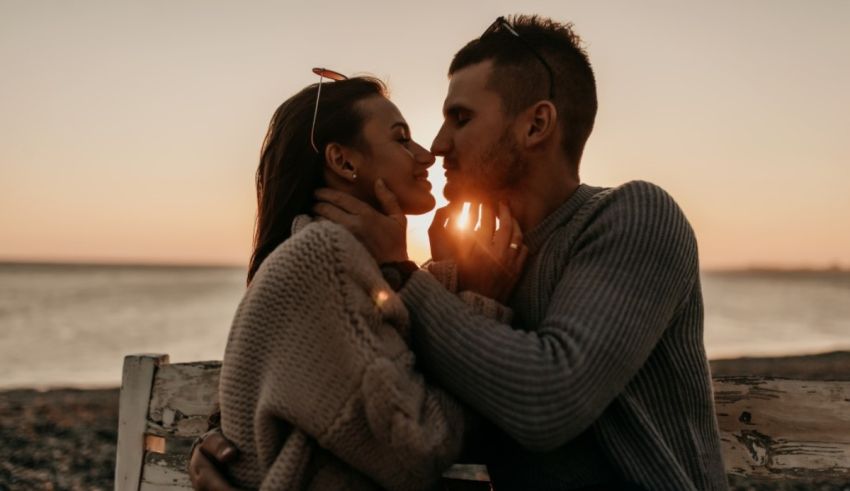 A couple kissing at sunset on a bench.