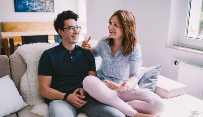 A young couple sitting on a couch talking to each other.