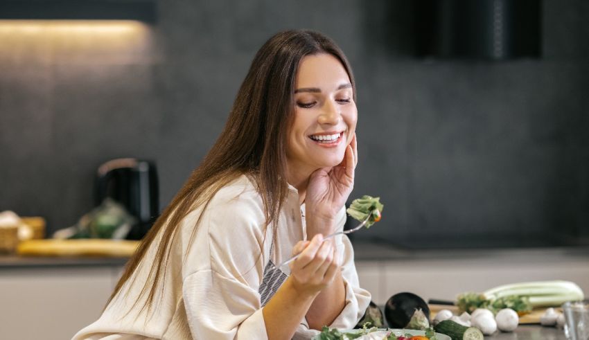 A woman is eating a salad in the kitchen.