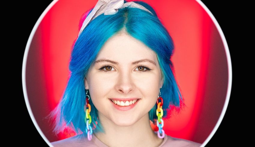 A woman with blue hair is smiling in front of a red background.