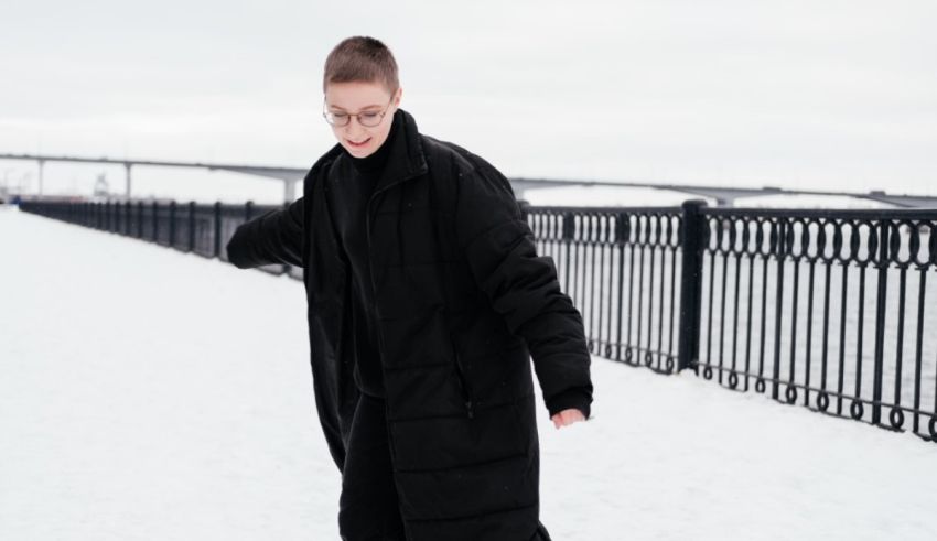 A woman in a black coat skates on a snowy sidewalk.