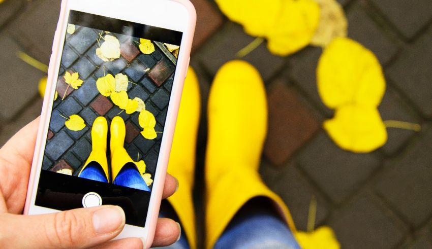 A person is taking a picture of yellow leaves on a sidewalk.