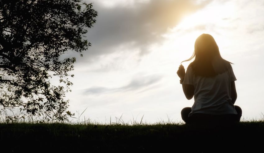 A woman is sitting on a grassy field with a tree in the background.