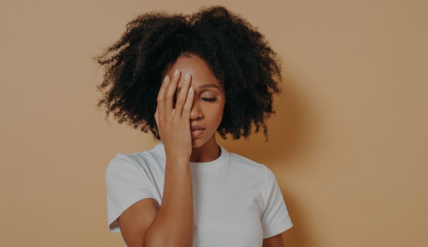 A woman with afro hair covering her face with her hands.