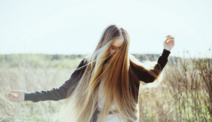 A girl with long blonde hair is standing in a field.