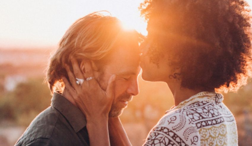 A man and woman kissing in front of a sunset.