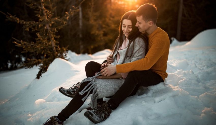 A couple sitting in the snow with a cell phone in their hands.
