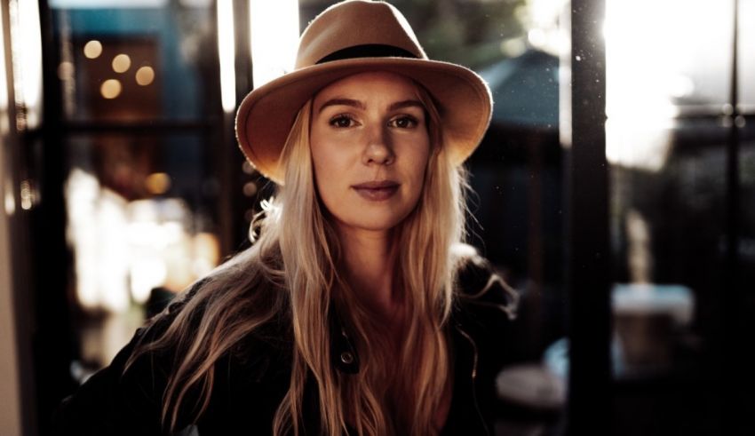 A woman in a hat is standing in front of a window.