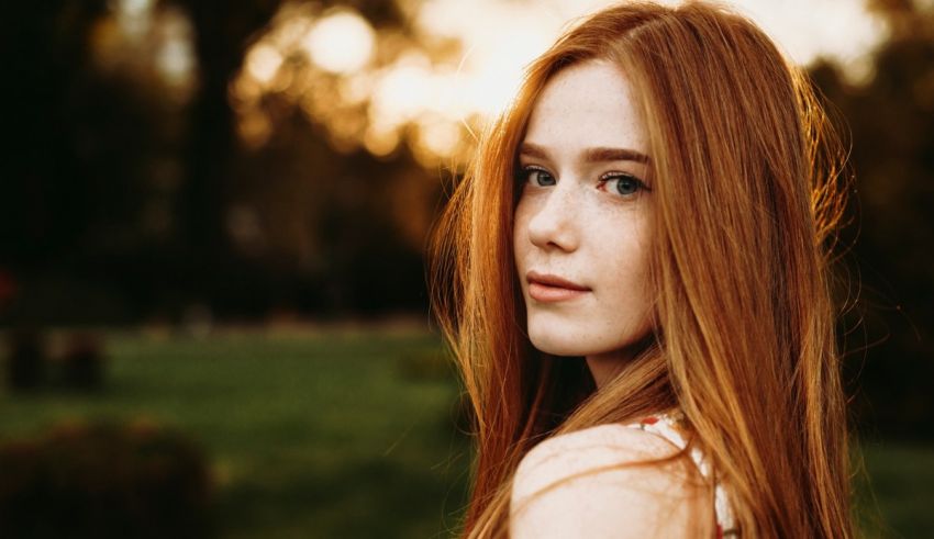 A girl with red hair is standing in a field.