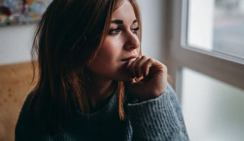 A woman looking out of a window with her hand on her chin.