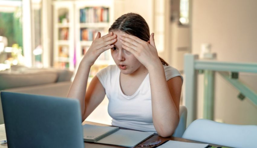 A young woman with her hands covering her eyes while working on a laptop.