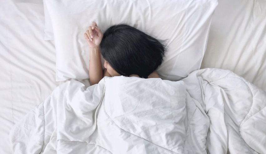 A woman laying in bed with a white blanket.