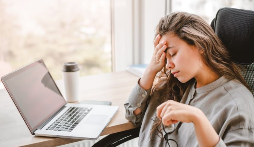 A woman is sitting in front of a laptop with her hand on her head.