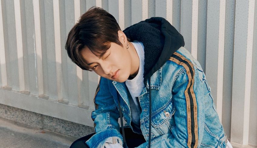 A young man in a denim jacket leaning against a wall.