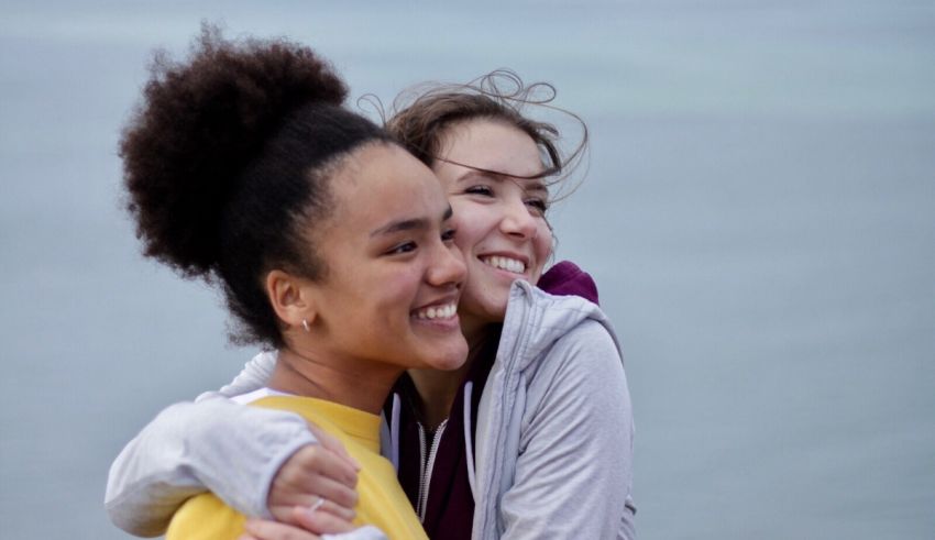Two girls hugging in front of a body of water.