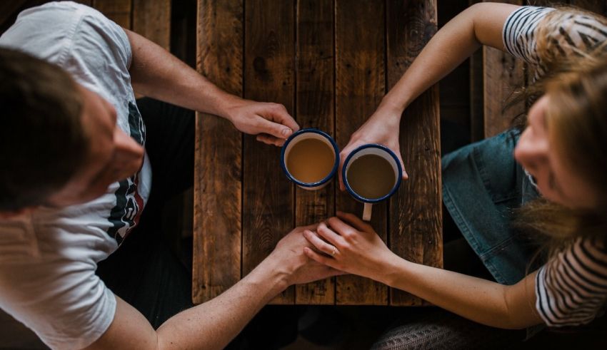 A man and woman are holding cups of coffee at a table.
