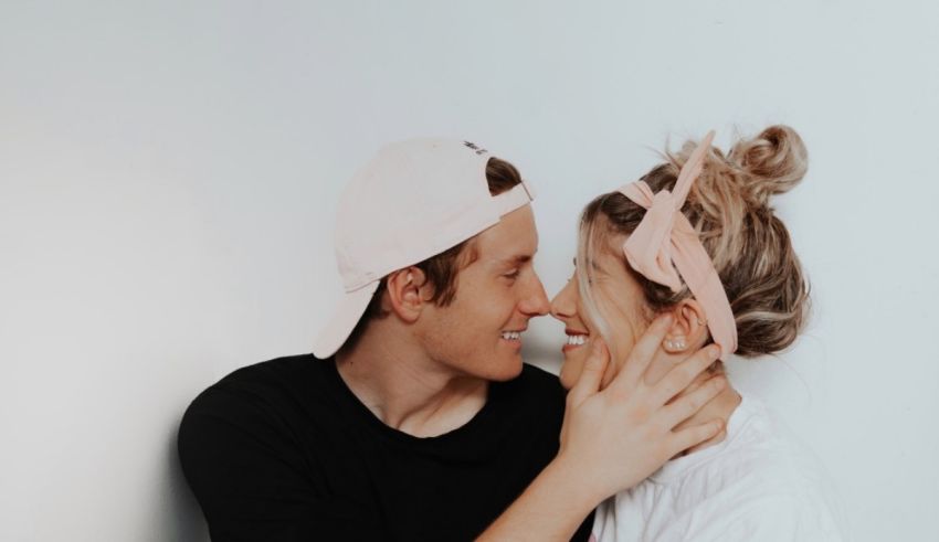 A man and woman kissing in front of a white wall.