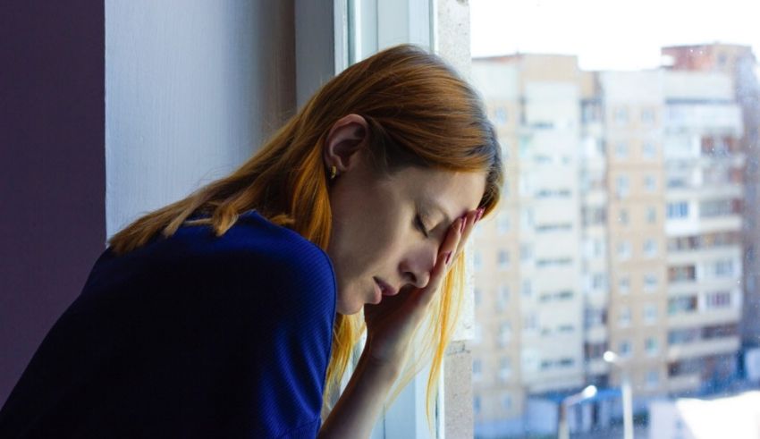 A woman is sitting on a window sill with her head in her hands.