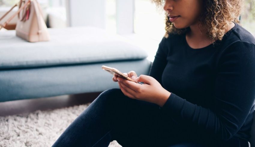 A woman sitting on the floor looking at her phone.