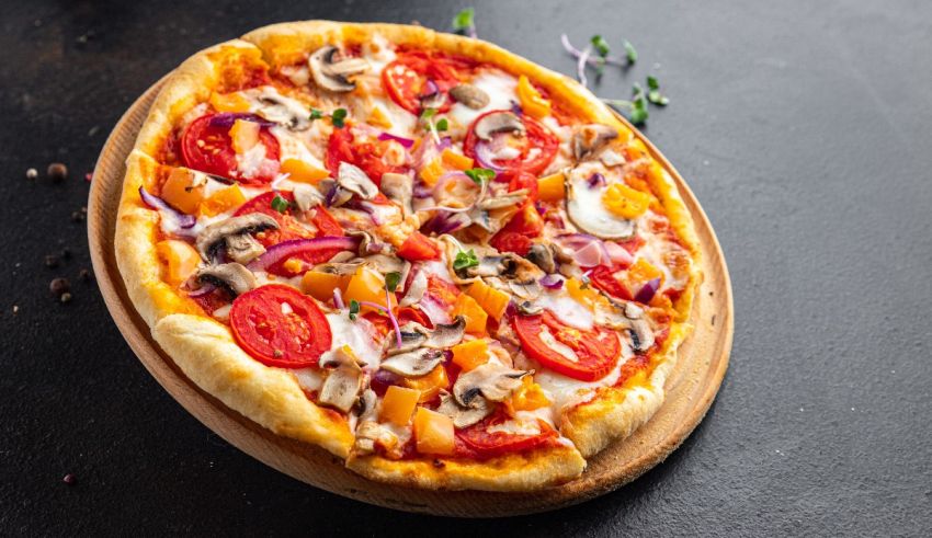 A pizza with tomatoes, onions and mushrooms on a wooden board.