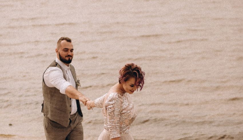 A man and woman holding hands and standing on a beach.