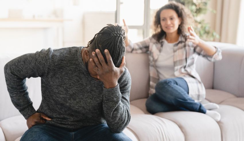 A man and woman sitting on a couch with their hands on their heads.