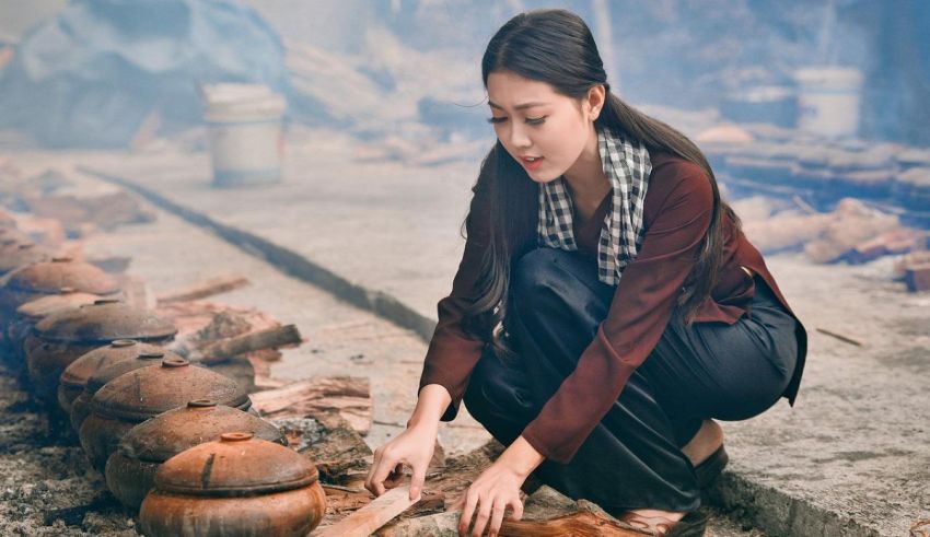 A woman is kneeling down next to a pile of wooden pots.