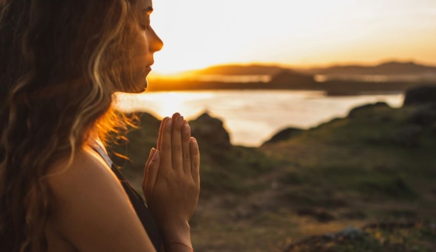 A woman is meditating in front of a lake at sunset.
