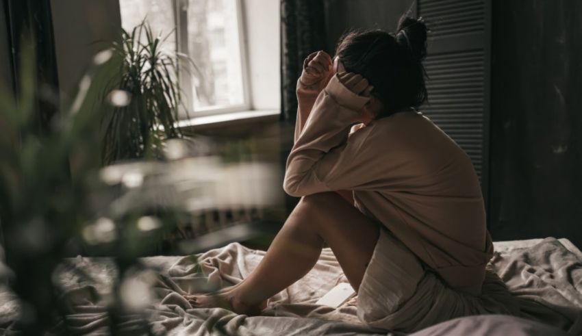 A woman sitting on a bed in front of a window.
