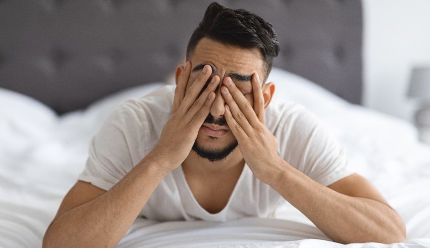 A man covering his eyes while laying on a bed.