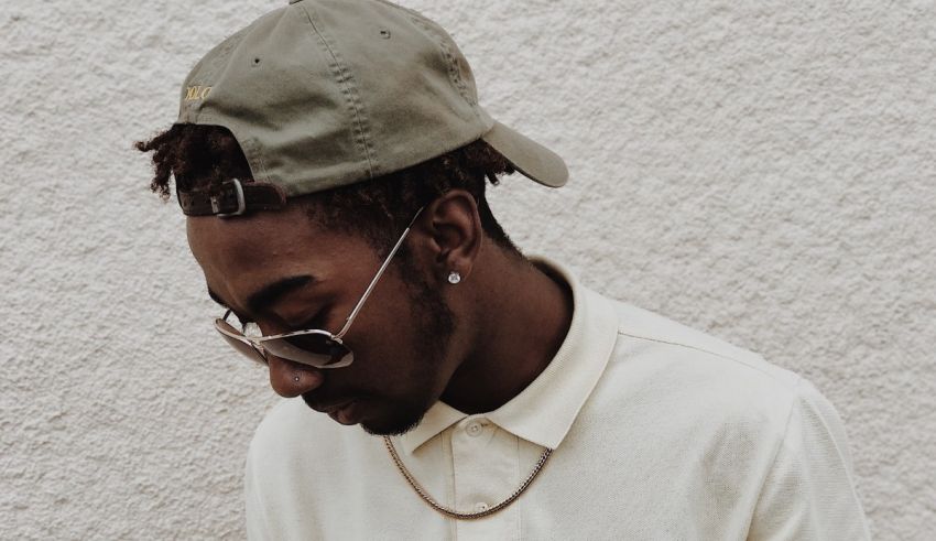 A man with dreadlocks and a hat leaning against a wall.