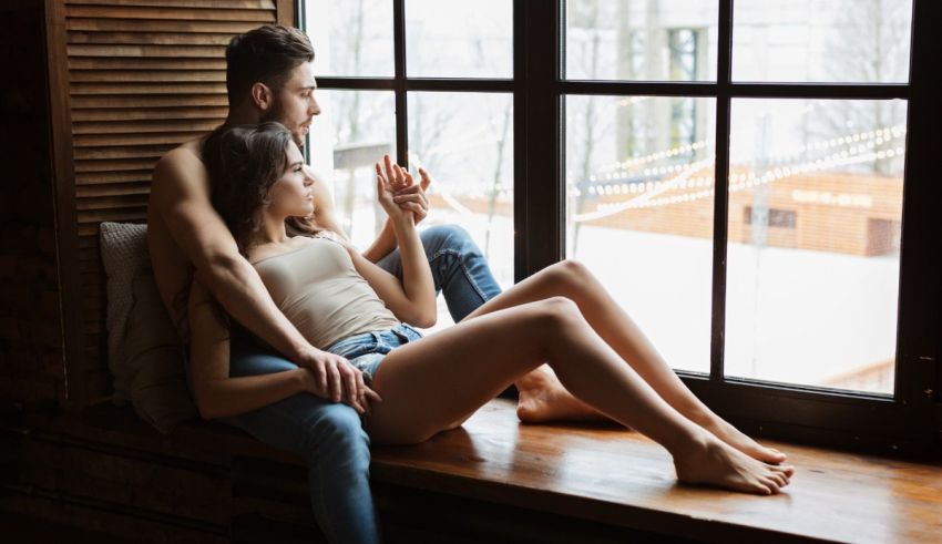 A man and woman sitting on a window sill.