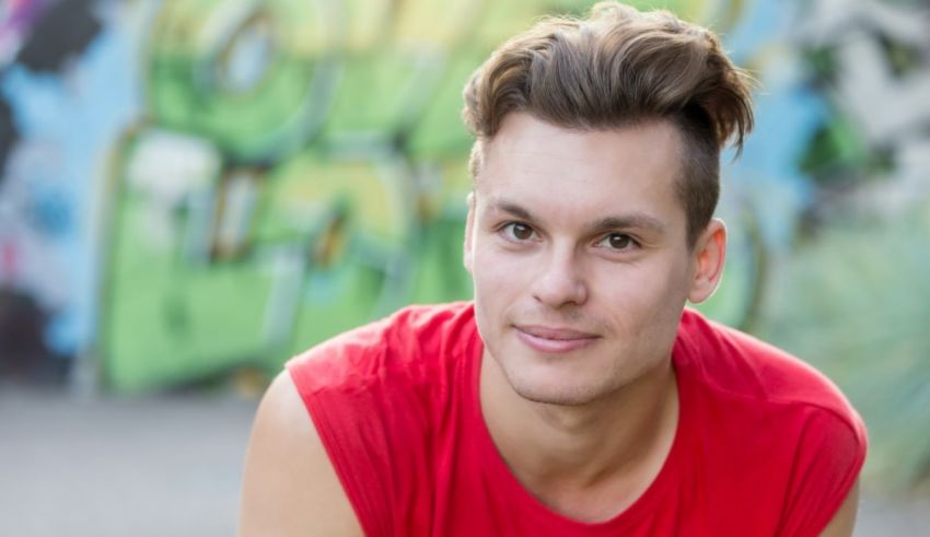 A young man in a red shirt is sitting in front of a graffiti wall.