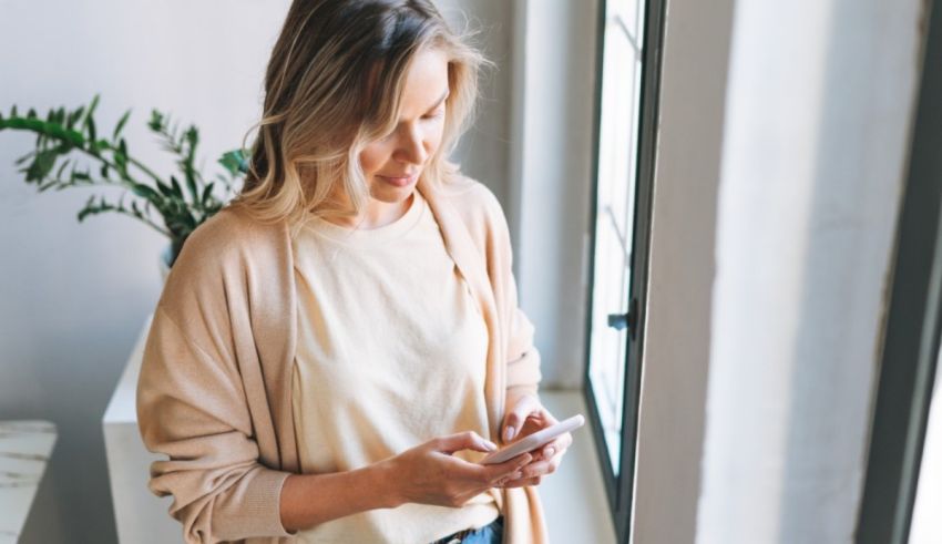 A woman is looking at her phone in front of a window.