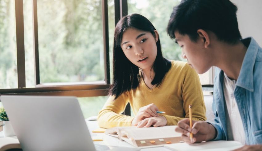 Two asian students working on a laptop in front of a window.