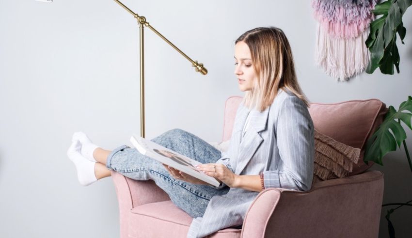 A woman is sitting in a pink chair reading a magazine.