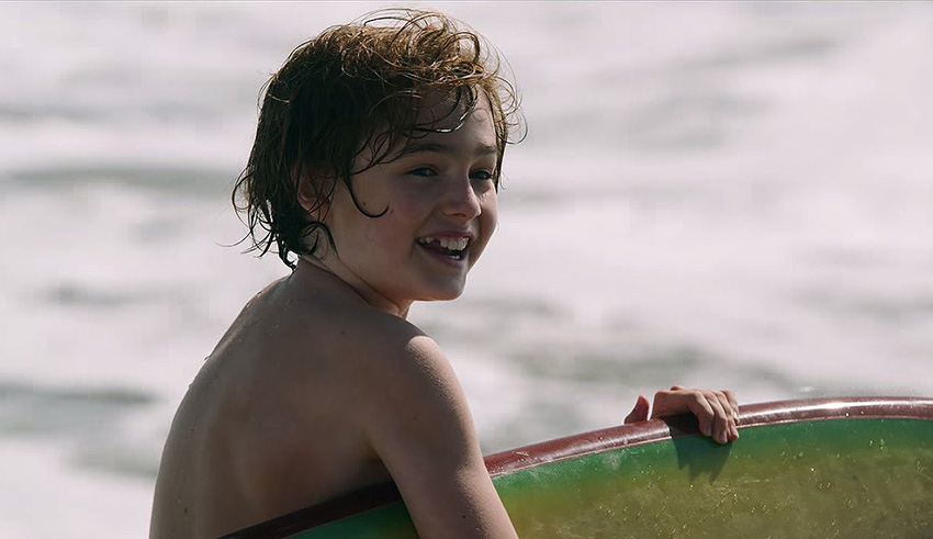 A young boy holding a surfboard in the ocean.