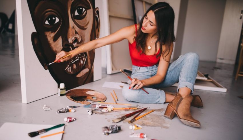 A woman is sitting on the floor painting a portrait.